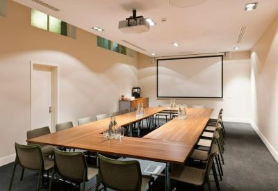 Professional meeting room with a large U-shaped wooden table and a projector screen.