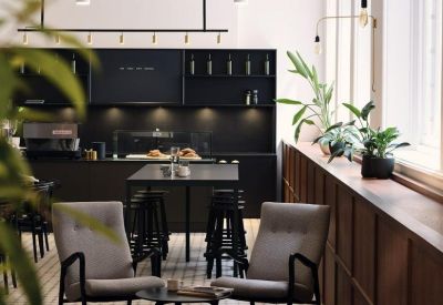 Modern communal kitchen and cafe area with black cabinetry, wooden accents, and green plants.