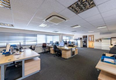 Spacious workspace with multiple wooden desks, computers, and overhead lighting.