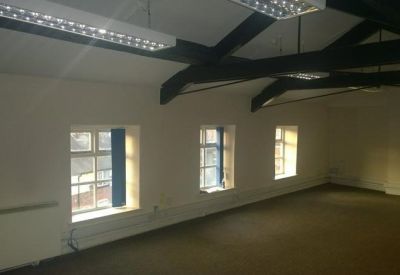 Large empty workspace with exposed dark wood ceiling beams and multiple windows.