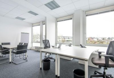 Bright shared workspace with multiple white desks and ergonomic chairs.