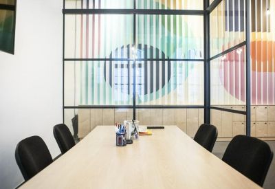 Professional meeting room with a light wood table, black chairs, and a glass partition wall.