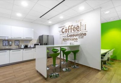 Sleek communal kitchen area with a white breakfast bar, green stools, and coffee-themed wall art.