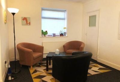 Brightly lit lounge area with warm orange tub chairs and a patterned geometric rug.