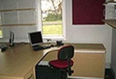 Bright private office suite with a corner desk and red swivel chair.