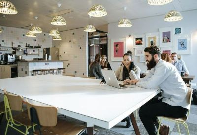 Coworking space with large white desk and industrial-style basket lighting.