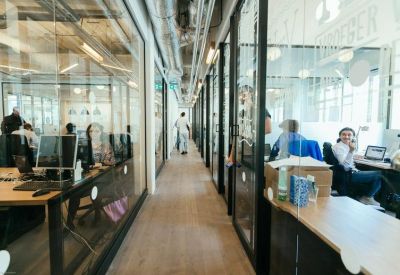 Glass-walled office corridor with view into private workstations.