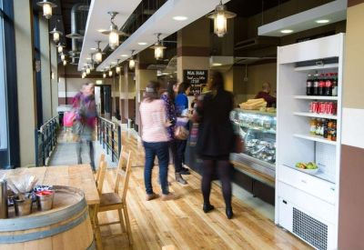 Communal cafe and breakout area with a deli counter, wooden floors, and modern lighting.