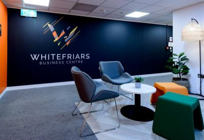 Branded reception area with grey armchairs, a white coffee table, and colorful stools.