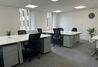 Bright open-plan office suite with white desks, grey storage units, and large windows.