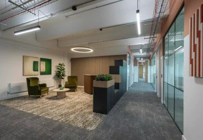 Reception area featuring velvet armchairs, a wooden coffee table, and a grey carpeted walkway.