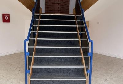 Symmetrical view of a central staircase with grey carpet treads and blue handrails.