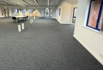 Spacious open-plan office area with grey carpeting and large windows.