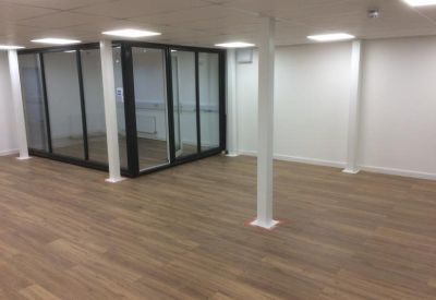 Large empty office area with wood-effect floors and a modern glass-partitioned meeting room.