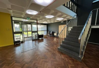 Building reception area with parquet flooring, a modern staircase, and seating.