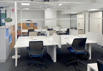 Open-plan coworking area with white shared desks and ergonomic blue chairs.