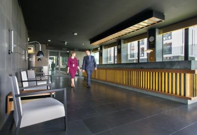 Modern lobby area with a long wooden reception desk and sleek grey flooring.