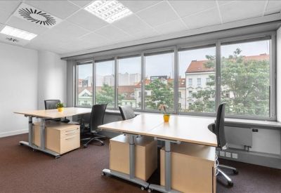 Bright private office with dual workstations and large windows overlooking the city.