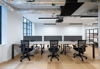 Open-plan office space with long desks, ergonomic mesh chairs, and industrial ceilings.