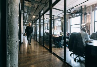 Industrial-style corridor with glass-partitioned offices and exposed concrete pillars.