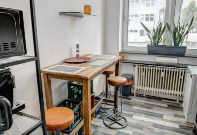 Bright dining nook featuring a wooden high table, leather stools, and potted plants by the window.
