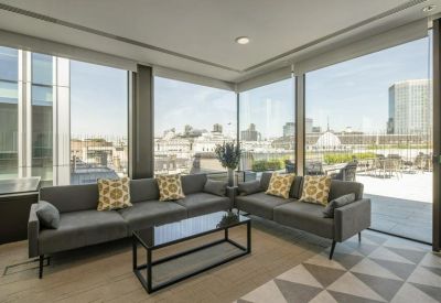Bright corner lounge area with grey sofas and floor-to-ceiling windows showing city views.