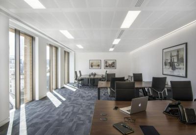 Spacious open-plan office with dark wood desks, black ergonomic chairs, and large windows.
