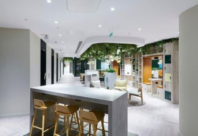 Modern lobby area with high-top tables, wooden stools, and lush greenery hanging from circular ceiling features.