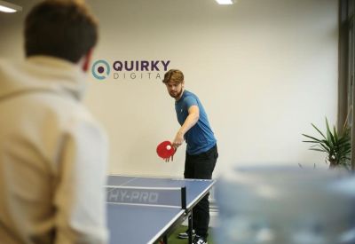 Breakout space with two people playing table tennis in front of a company logo.