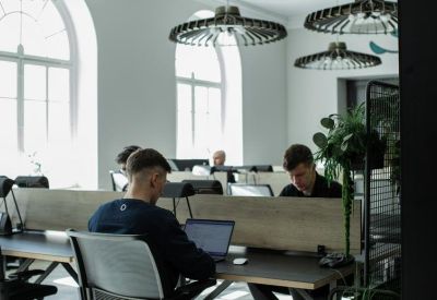 Bright open-plan office with people working at wooden desks under decorative circular lights.