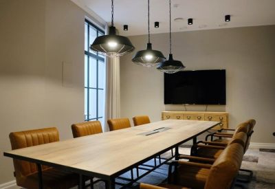Modern conference room with a long wooden table, tan leather chairs, and industrial pendant lights.