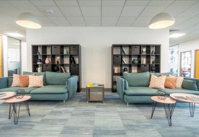 Spacious communal lounge with teal sofas, wooden coffee tables, and shelving units.