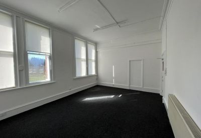 Bright, empty corner office with black carpeting and three large windows with blinds.