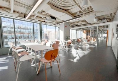 Bright dining area with white tables, orange chairs, and exposed ceiling pipes.