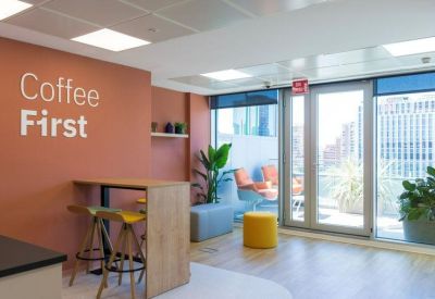 Vibrant breakroom featuring an orange accent wall with Coffee First signage and yellow stools.