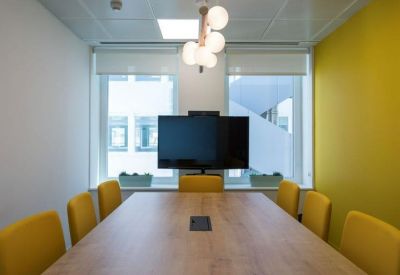 Professional meeting room with a wooden table, yellow chairs, and a wall-mounted screen.