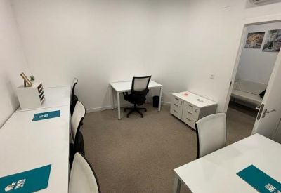 Bright multi-desk office space with white workstations and teal desk mats.