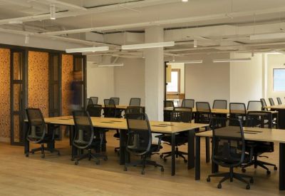 Open-plan office area with several long wooden desks and ergonomic chairs.