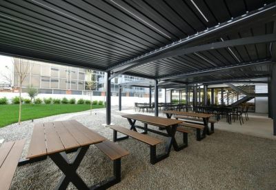 Outdoor communal area under a black pergola with several wooden picnic tables.