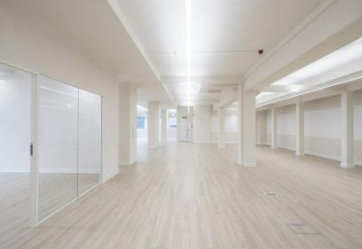 Spacious open-plan office floor with light wood flooring and glass partitions.