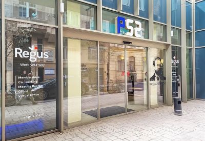 Wide exterior of the modern glass building entrance with sliding doors and building signage.