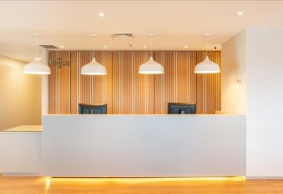 Bright reception area with a long white desk, wooden feature wall, and hanging pendant lights.