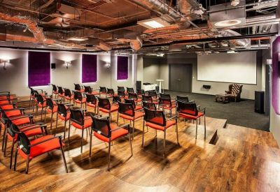 Spacious presentation room with rows of red chairs and a large projector screen.