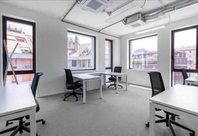 Bright shared office with white desks, ergonomic black chairs, and large windows overlooking the city.