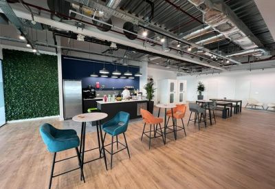 Spacious communal breakout area with high tables, blue and orange velvet stools, and a green living wall.