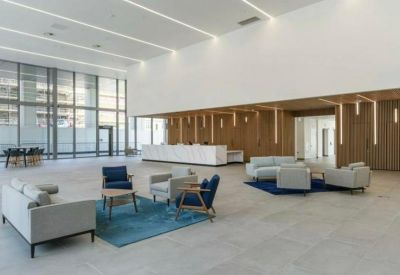 Bright, high-ceilinged reception lobby with grey sofas, blue armchairs, and a white marble desk.
