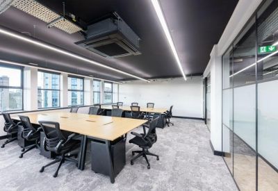 Spacious open-plan office with large wooden desks, ergonomic chairs, and floor-to-ceiling windows.