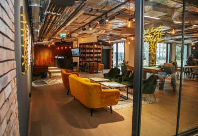 Spacious lounge area with yellow velvet sofas, green armchairs, and an industrial-style ceiling.