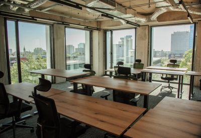 Sunlit open-plan office with wooden desks, ergonomic chairs, and large windows overlooking the city.
