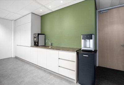 Office kitchen area featuring white cabinetry, a green accent wall, and coffee machine.